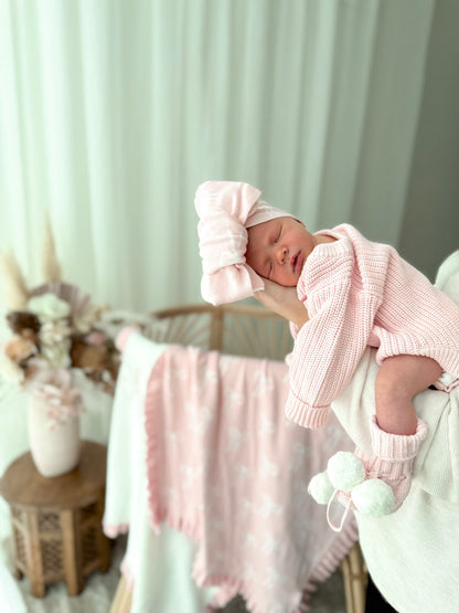 Newborn baby in pink outfit and hat sleeping on a chair with a soft blanket.