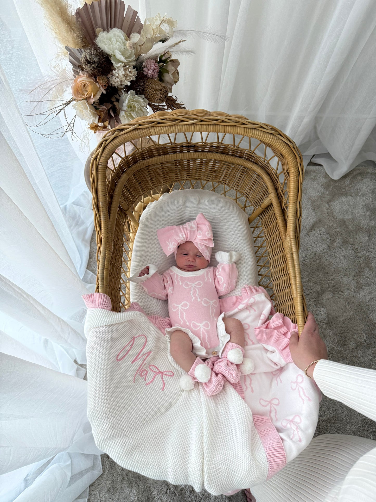 Newborn baby in a wicker crib with pink outfit and floral decorations.