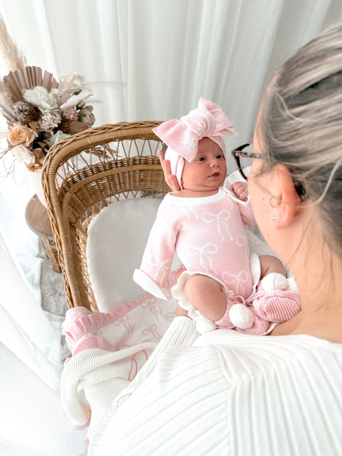 Baby in pink outfit with a bow sitting on a woman's lap, surrounded by decorative elements.