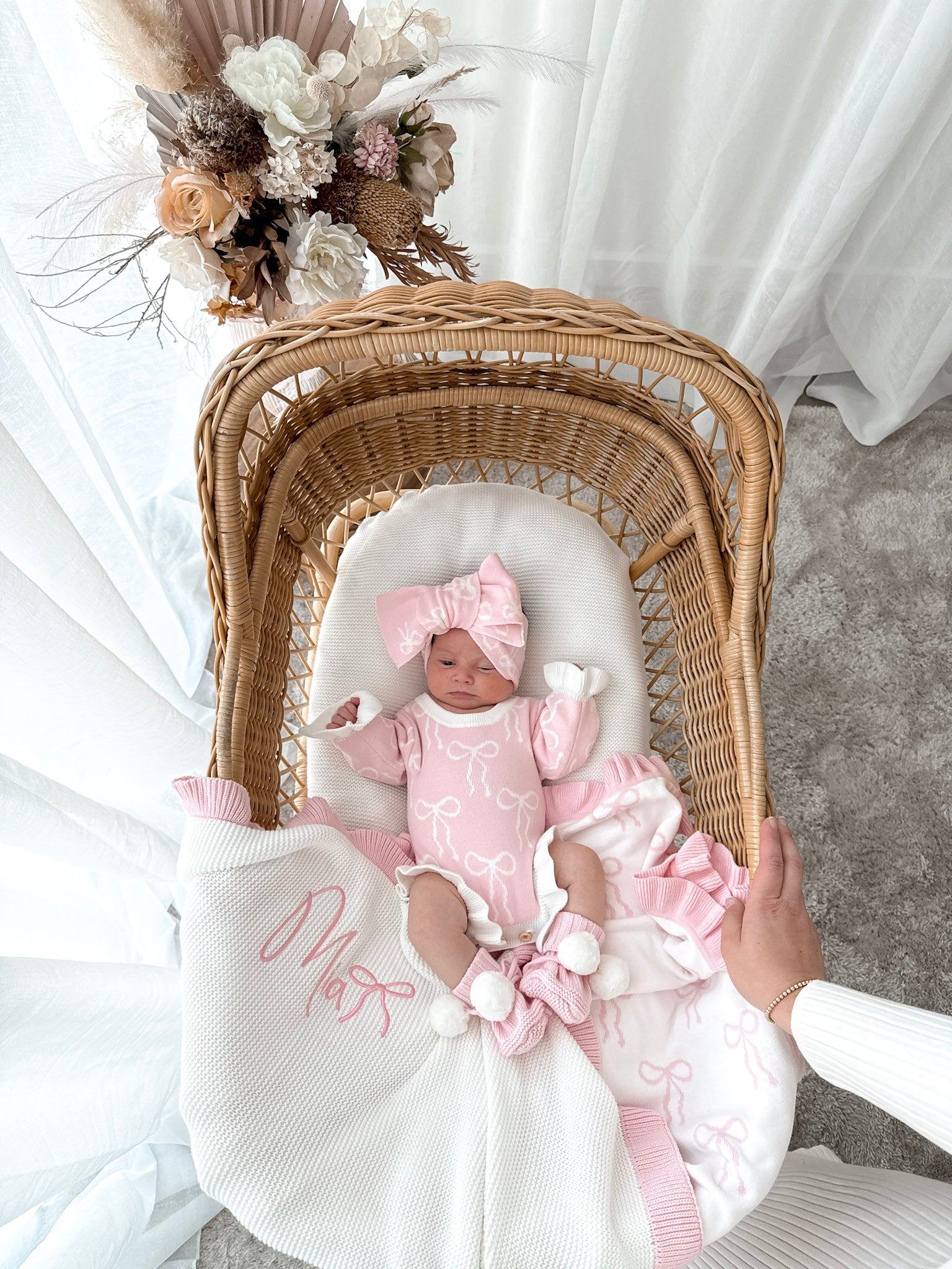 Newborn baby in a wicker crib with pink outfit and floral decorations.