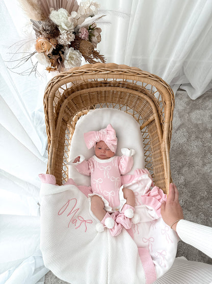 Newborn baby in a wicker crib with pink outfit and floral decorations.