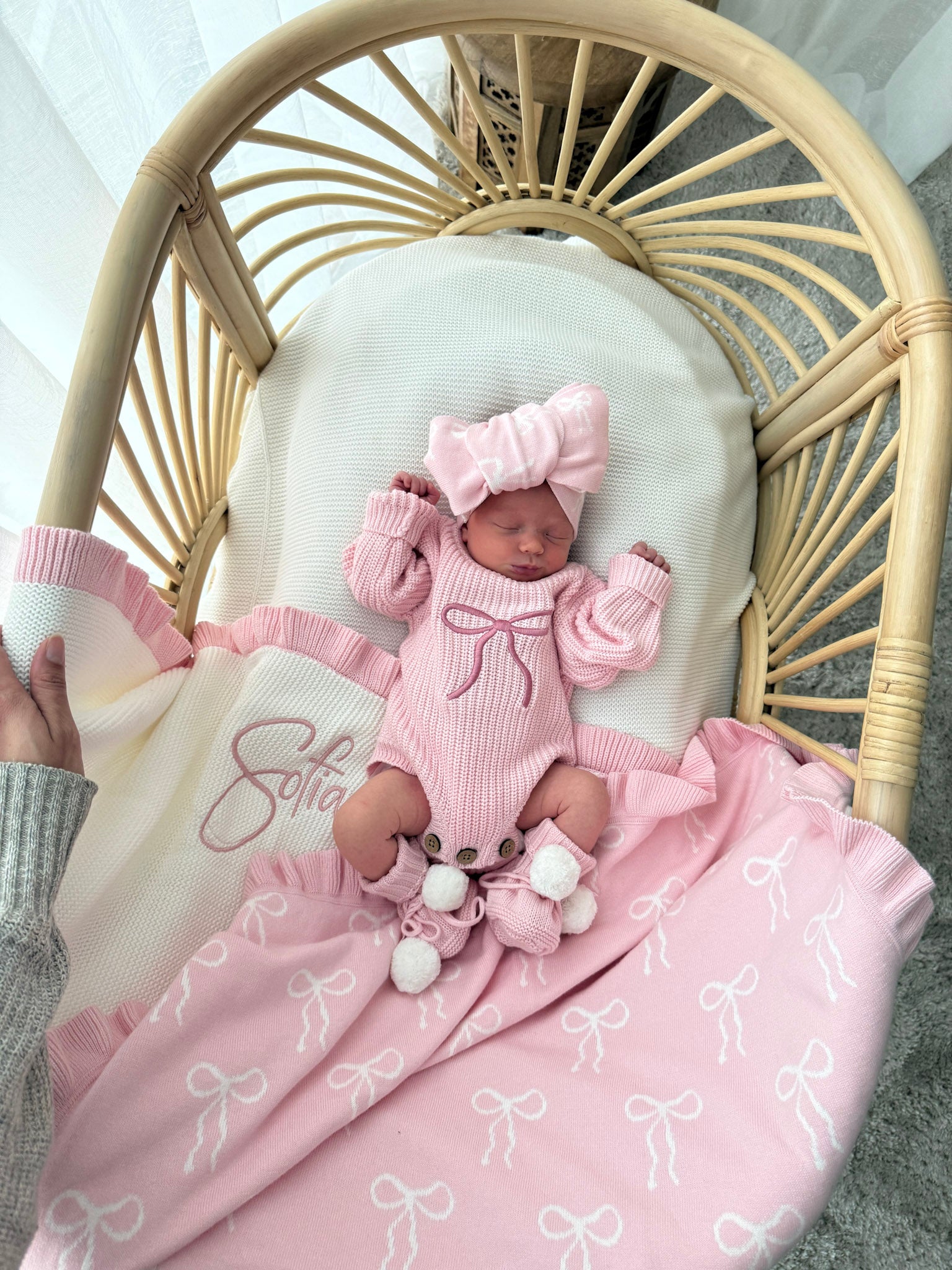 Newborn baby in pink outfit with matching headband in a crib with pink blanket.