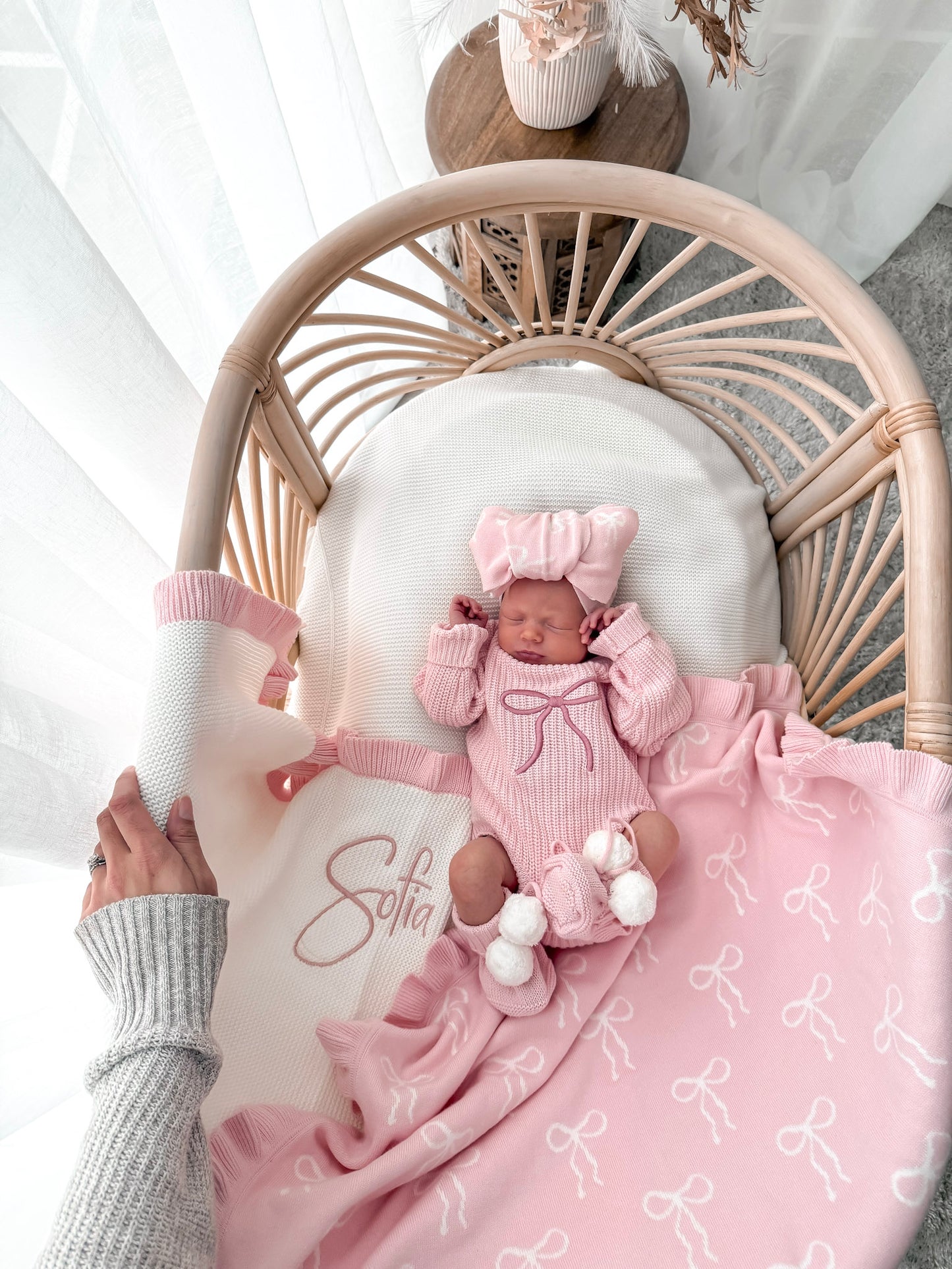 Newborn baby in pink outfit with matching blanket on a wicker chair