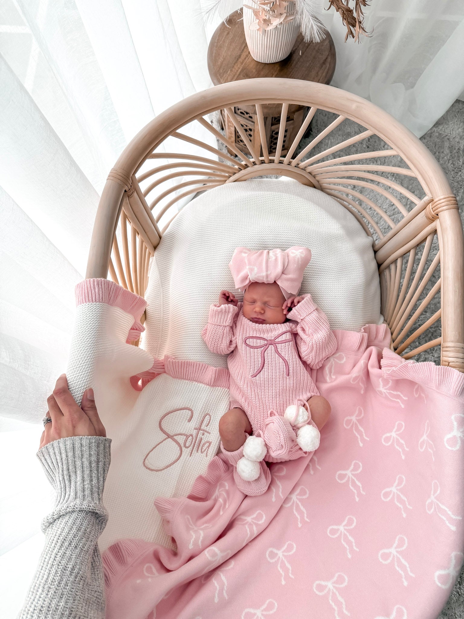 Newborn baby in pink outfit with matching blanket on a wicker chair