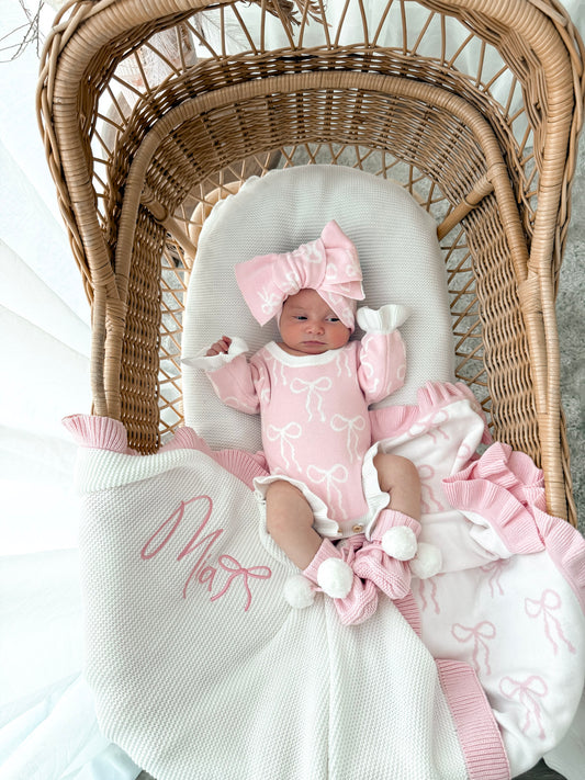 Newborn baby in a wicker crib with pink and white outfit and accessories.
