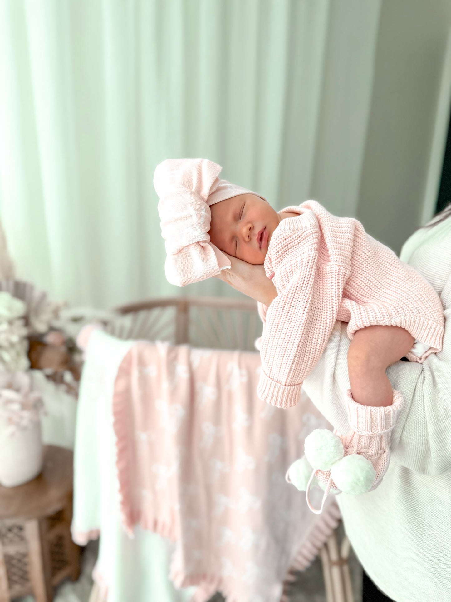 Newborn baby in pink outfit with matching headband in a nursery setting