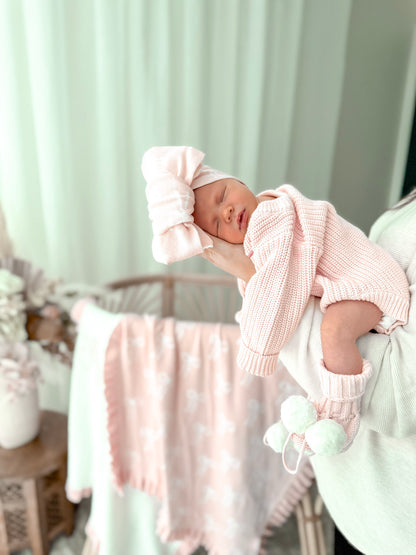 Newborn baby in pink outfit with matching headband in a nursery setting