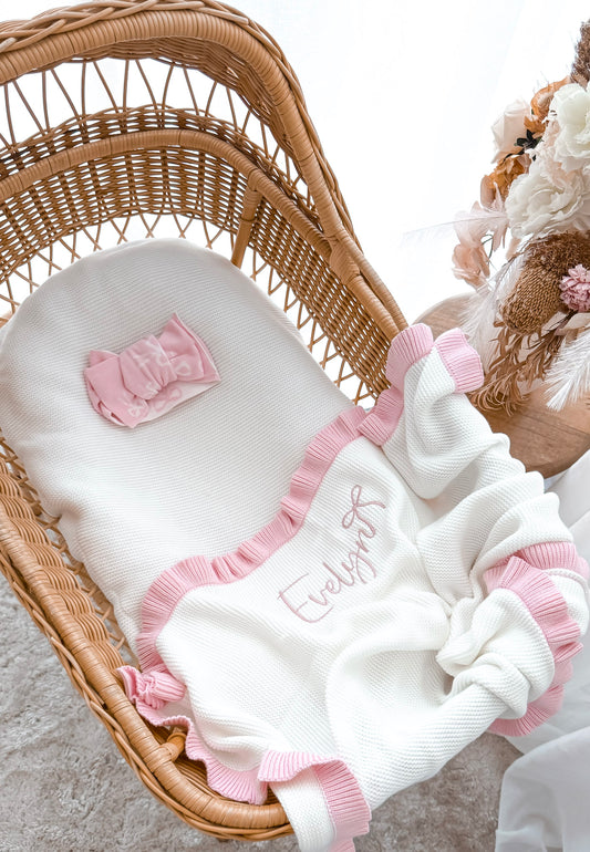 Baby blanket with pink trim and embroidered name in a wicker crib