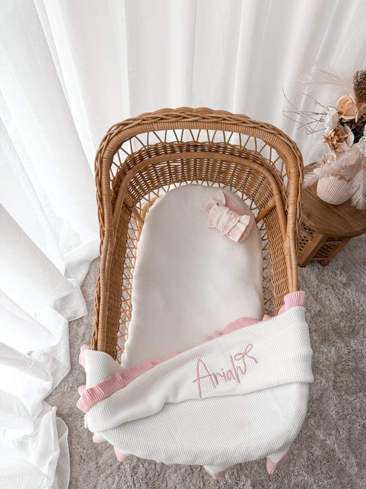 Personalised blanket that is white with pink frills on a wicker basket 
