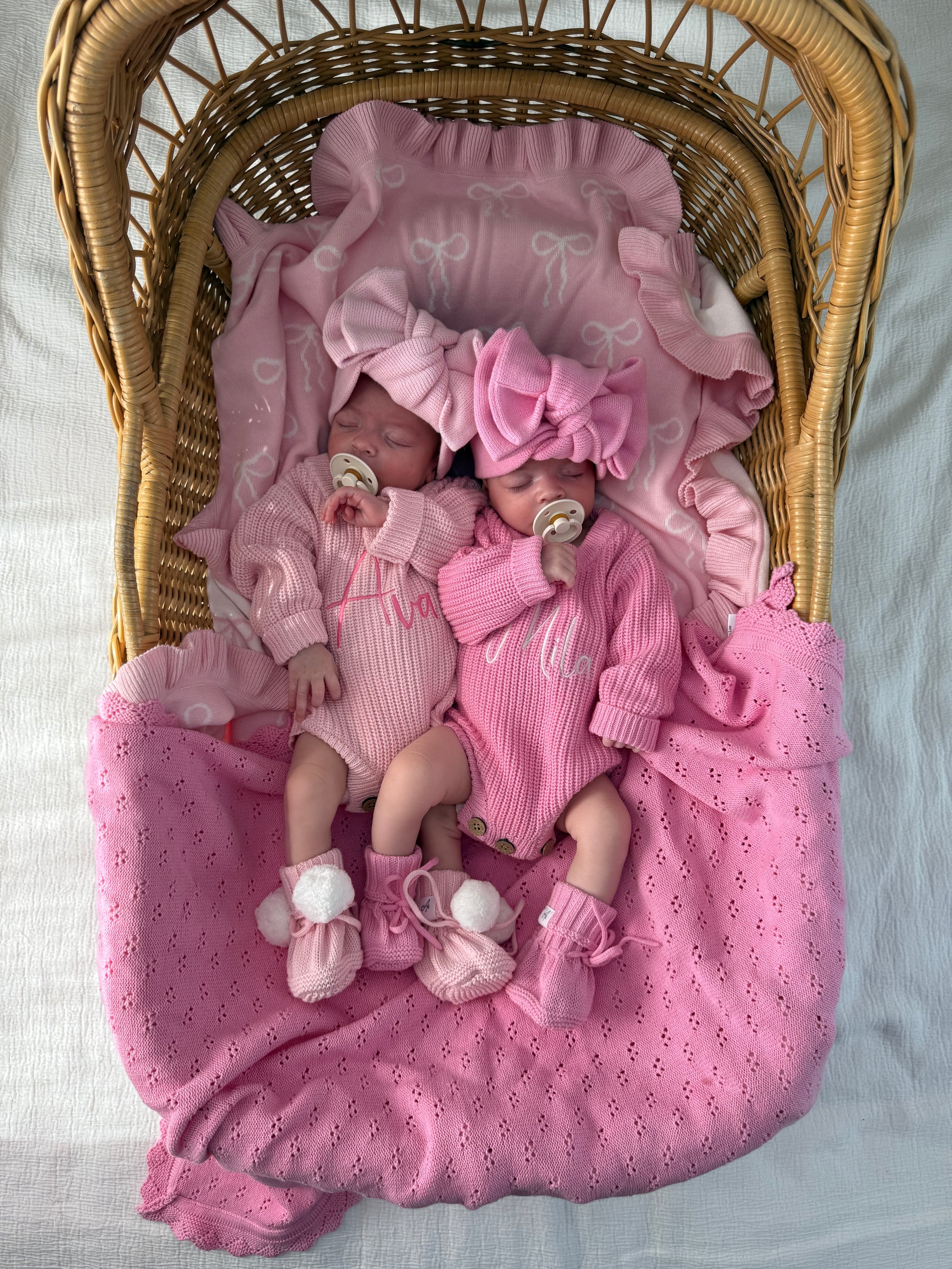 Newborn baby in a pink outfit lying on a pink blanket in a wicker basket.