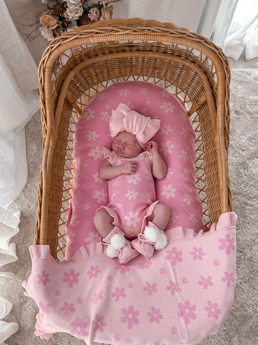 Newborn baby in a wicker crib with pink bedding and floral decorations.